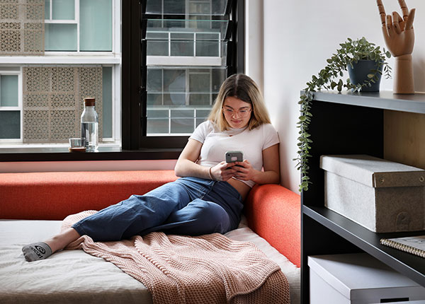 Student sitting on her bed next to window in modern apartment.