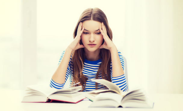 woman looking at open books with hands on her head